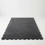 Front facing view of the Aether Dior grey wool rug with scalloped edges displayed on a white studio floor.