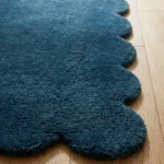 Close-up angled view of the Aqualene runner rug on a wooden floor, highlighting the dense, plush hand-tufted New Zealand wool and viscose silk texture and the gracefully contoured deep teal blue scalloped border.