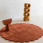 Burnt Clay circular terracotta rug with scalloped edges displayed in a minimalist room setting with wooden art.