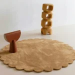 Camel Dawn round wool rug with scalloped edges displayed in a modern minimalist room setting with wooden abstract decor.