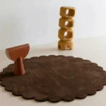 Cocoa Crest round wool rug with scalloped edges displayed in a modern minimalist room setting with wooden abstract decor.