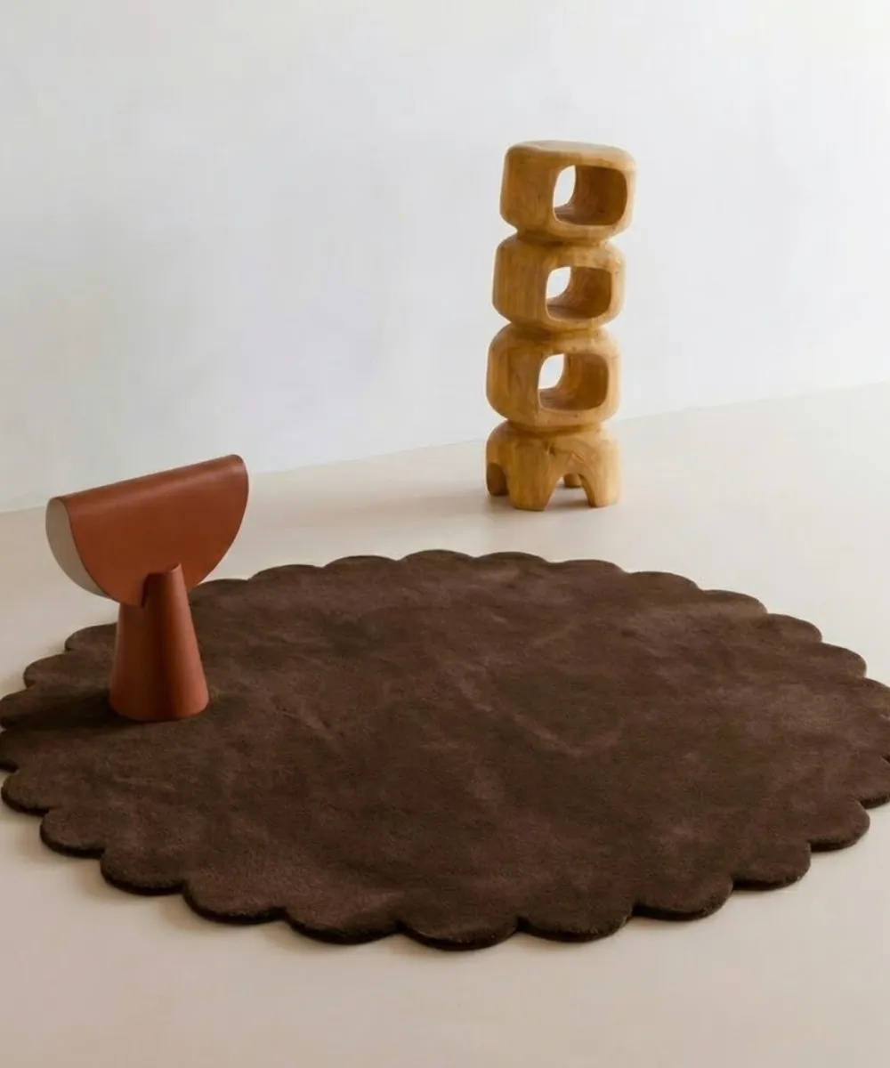 Cocoa Crest round wool rug with scalloped edges displayed in a modern minimalist room setting with wooden abstract decor.