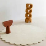 Cream Halo round wool rug with scalloped edges displayed in a modern minimalist room setting with wooden abstract decor.
