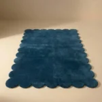 Front facing view of the Deep Marine blue wool rug with scalloped edges displayed on a beige studio floor.