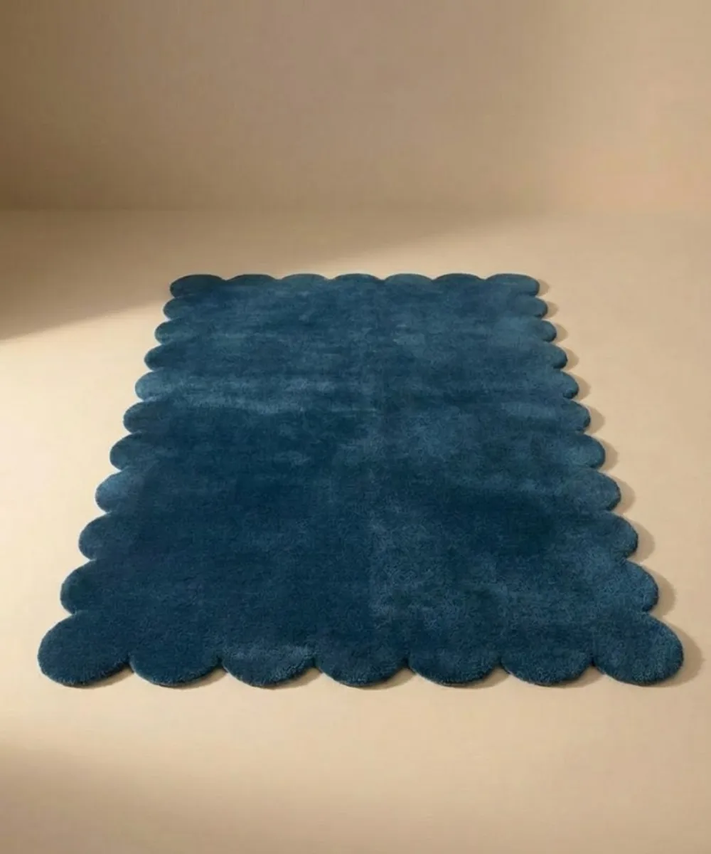 Front facing view of the Deep Marine blue wool rug with scalloped edges displayed on a beige studio floor.