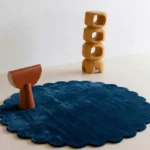 Deepstone circular dark blue rug with scalloped edges displayed in a minimalist room setting with wooden art.