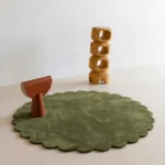Forest Mirage round green hand tufted wool rug with scalloped edges displayed in a modern minimalist room setting with wooden decor.