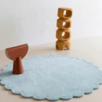 Ice Whisper circular blue rug with scalloped edges styled in a bright modern room with wooden art pieces.