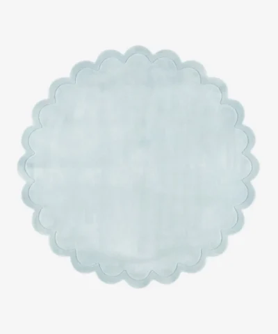 Top down flat lay view of the Ice Whisper round rug showing the soft light blue wool color and scalloped border.