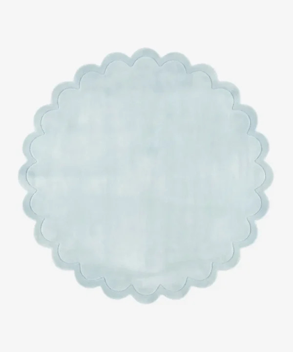 Top down flat lay view of the Ice Whisper round rug showing the soft light blue wool color and scalloped border.