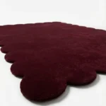 Angled perspective view of the Merlot Plum rectangular wool rug displaying the deep wine color and elegant scalloped border.