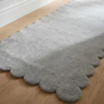 Close-up angled view of the Moonhaze runner rug on a wooden floor, highlighting the dense, plush hand-tufted New Zealand wool and viscose silk texture and the gracefully contoured light grey scalloped border.