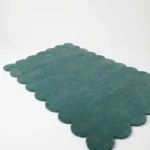 Angled perspective view of the Ocean Mist rectangular wool rug displaying the soft teal color and elegant scalloped border.