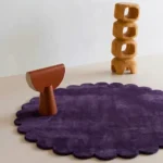 Plum Eclipse round purple rug with scalloped borders styled in a contemporary room with wooden art objects.