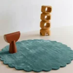 Sagewave round green rug with scalloped edges styled in a minimalist room with modern wooden art pieces.