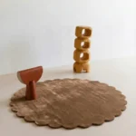 Sandstone round wool rug with scalloped edges displayed in a modern minimalist room setting with wooden abstract decor.
