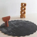 Slate Cloud circular grey rug with scalloped edges styled in a modern minimalist room with wooden art pieces.