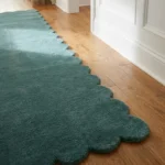 Close-up angled view of the Tidefall runner rug on a wooden floor, highlighting the dense, plush hand-tufted New Zealand wool and viscose silk texture and the gracefully contoured muted teal blue scalloped border.