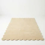 Angled perspective view of the Vanilla Crest rectangular wool rug displaying the soft cream color and elegant scalloped border.