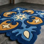 Close-up low angle view of the Azure Heirloom rug, showcasing the plush hand-tufted wool texture, the deeply carved lines defining the blue and gold geometric floral patterns, and the intricately contoured scalloped border.