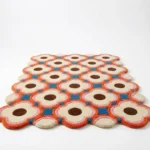 Low angle perspective of the Blush Bloom rug showing the retro pink and blue geometric floral pattern and the decorative scalloped border on a white floor.