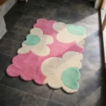 Perspective view of the Blush Petalia rug placed on a dark tiled floor, featuring a retro oversized floral pattern in soft pink, cream, and mint green, finished with a petal-contoured scalloped edge.