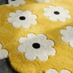 Close-up low angle view of the Butter Pop rug, showcasing the plush hand-tufted wool texture, the deeply carved white flowers with black centers, and the intricately contoured yellow scalloped border.