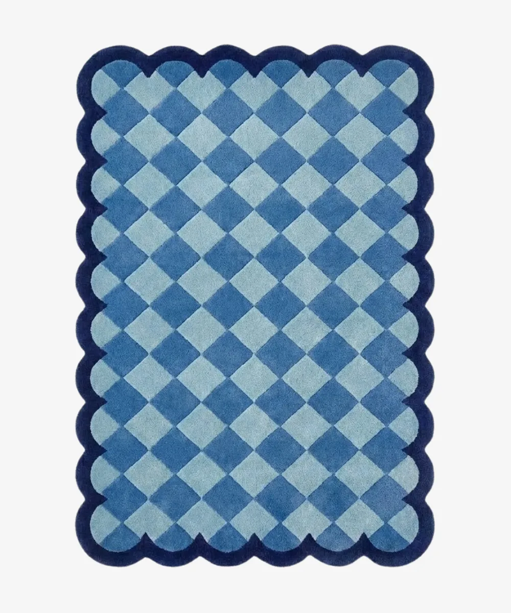 Top down view of the Coastal Current rug featuring a diamond checkerboard pattern in soothing shades of light and slate blue, framed by a dark blue scalloped border.