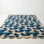 Low angle perspective of the Coastal Mosaic wool rug placed on a white floor, showcasing the rhythmic geometric motif and soft blue tones.