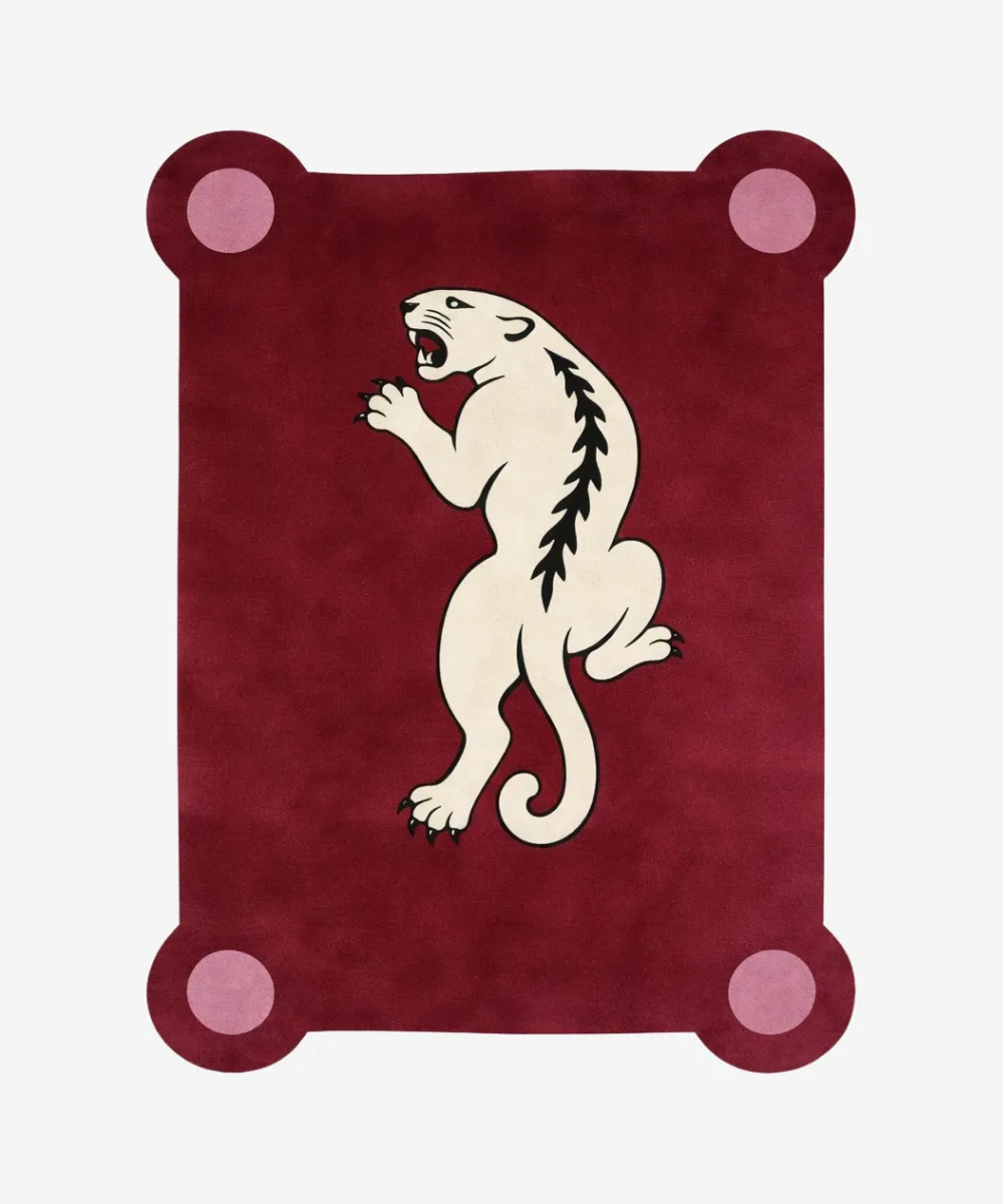 Top down view of the Crimson Prowl rug featuring a deep maroon wool background with a stylized white panther climbing design and pink circular corner accents.