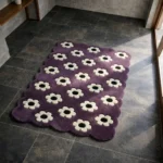 Perspective view of the Daisy Night rug placed on a dark tiled floor, featuring a deep purple background adorned with a repeating retro pattern of white daisies with black centers, finished with a decorative scalloped edge.
