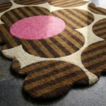 Close-up low angle view of the Dusky Bloom rug, showcasing the plush hand-tufted wool texture, the deeply carved lines separating the brown striped petals from the solid pink centers, and the intricately contoured scalloped border.