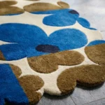 Close-up low angle view of the Earthen Dusk rug, showcasing the plush hand-tufted wool texture, the deeply carved lines separating the bold blue and brown flower petals, and the intricately contoured scalloped border.