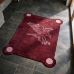 High angle view of the Ember Crest rug placed on a dark tiled floor, featuring a deep burgundy background with a contrasting light pink eagle illustration and unique rounded corners containing pink circles.