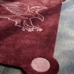 Close-up detail of the Ember Crest rug, highlighting the plush hand-tufted wool texture, the embossed pink line-art of a flying eagle, and the distinctive rounded corner with a solid pink accent circle.