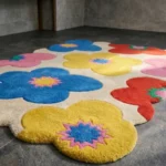 Close-up low angle view of the Flora Fiesta rug, showcasing the plush hand-tufted wool texture, the deeply carved lines separating the vibrant flower petals and their distinct jagged centers, and the uniquely contoured scalloped border.