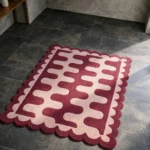High angle view of the Garnet Loop rug featuring a bold interlocking wavy pattern in deep burgundy red and soft pink, finished with a decorative scalloped edge.