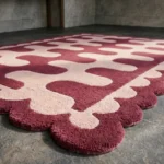 Close-up detail of the Obsidian Grid rug, highlighting the plush hand-tufted wool texture, the distinctive light pink and pink wavy interlocking design, and the intricate deep red scalloped border.