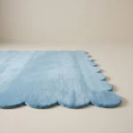 Low angle perspective of the Glacier Haze rug showing the soft light blue wool texture and the elegant scalloped border placed on a white floor.
