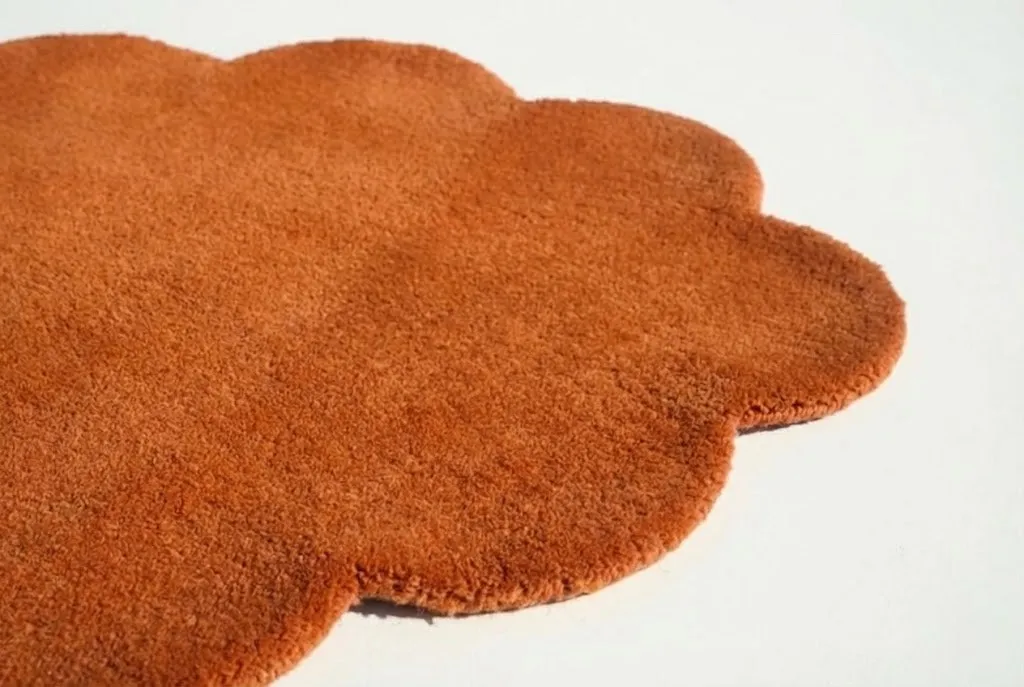 Shop Rugs by Shape navigation guide displayed on a wooden table, featuring categories for Rectangular, Round, Runner, and Oval designs. Includes samples of dense New Zealand wool textures and hand-tufted color swatches.