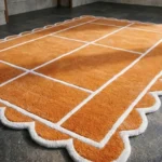 Close-up low angle view of the Hearth Grid rug, highlighting the dense, plush hand-tufted New Zealand wool texture, the embossed white grid lines, and the intricately carved white scalloped border.