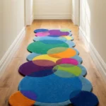 Eye level view of the Indigo Carnival runner rug placed in a bright hallway, showcasing its vibrant overlapping circle pattern in blues, greens, and purples with scalloped edges.