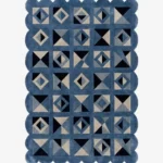 Top down view of the Indigo Tessellate rug against a white background, featuring a repeating patchwork pattern of geometric squares, triangles, and diamonds in solid shades of indigo blue, grey, and black, framed by a continuous blue scalloped border.