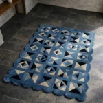 Close-up angled view of the Indigo Tessellate rug, highlighting the dense hand-tufted New Zealand wool texture, the deeply carved lines separating the geometric blue, grey, and black patchwork shapes, and the intricately contoured scalloped edge.