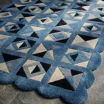 Perspective view of the Indigo Tessellate rug placed on a dark tiled floor, showcasing the bold geometric patchwork design and the structured blue scalloped border illuminated by natural sunlight.