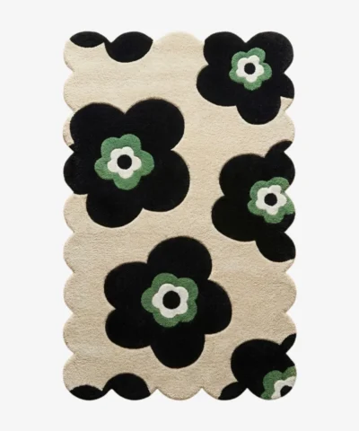 Top down flat lay of the Inked Botanica rug featuring bold black floral silhouettes with sage green centers on a beige wool background.