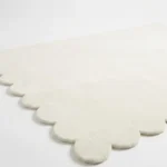 High angle close up view of the Ivory Drift rug showing the soft cream wool texture and the clean finish of the hand cut scalloped border.