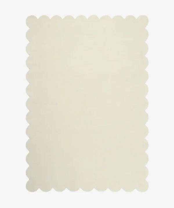 Top down flat lay of the Ivory Drift hand tufted rug featuring a solid off white color and decorative wavy edges isolated on a white background.
