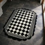 Perspective view of the Ivory Lattice rug featuring a repeating dark brown geometric chain-link pattern on a soft cream background, framed by a continuous dark brown scalloped edge.