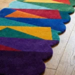 Close-up angled view of the Jewel Shards runner rug on a wooden floor, highlighting the dense, plush hand-tufted New Zealand wool and viscose silk texture, the deeply carved lines separating the colorful geometric blocks, and the intricately contoured scalloped border.